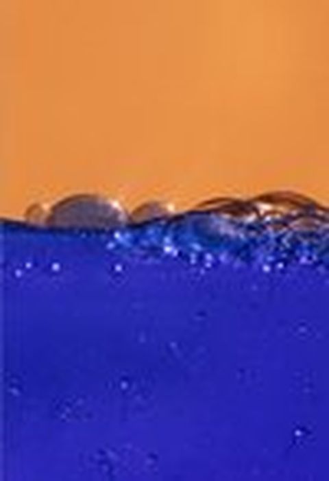 Gotas de agua en la superficie de un líquido de color azul oscuro con fondo anaranjado.